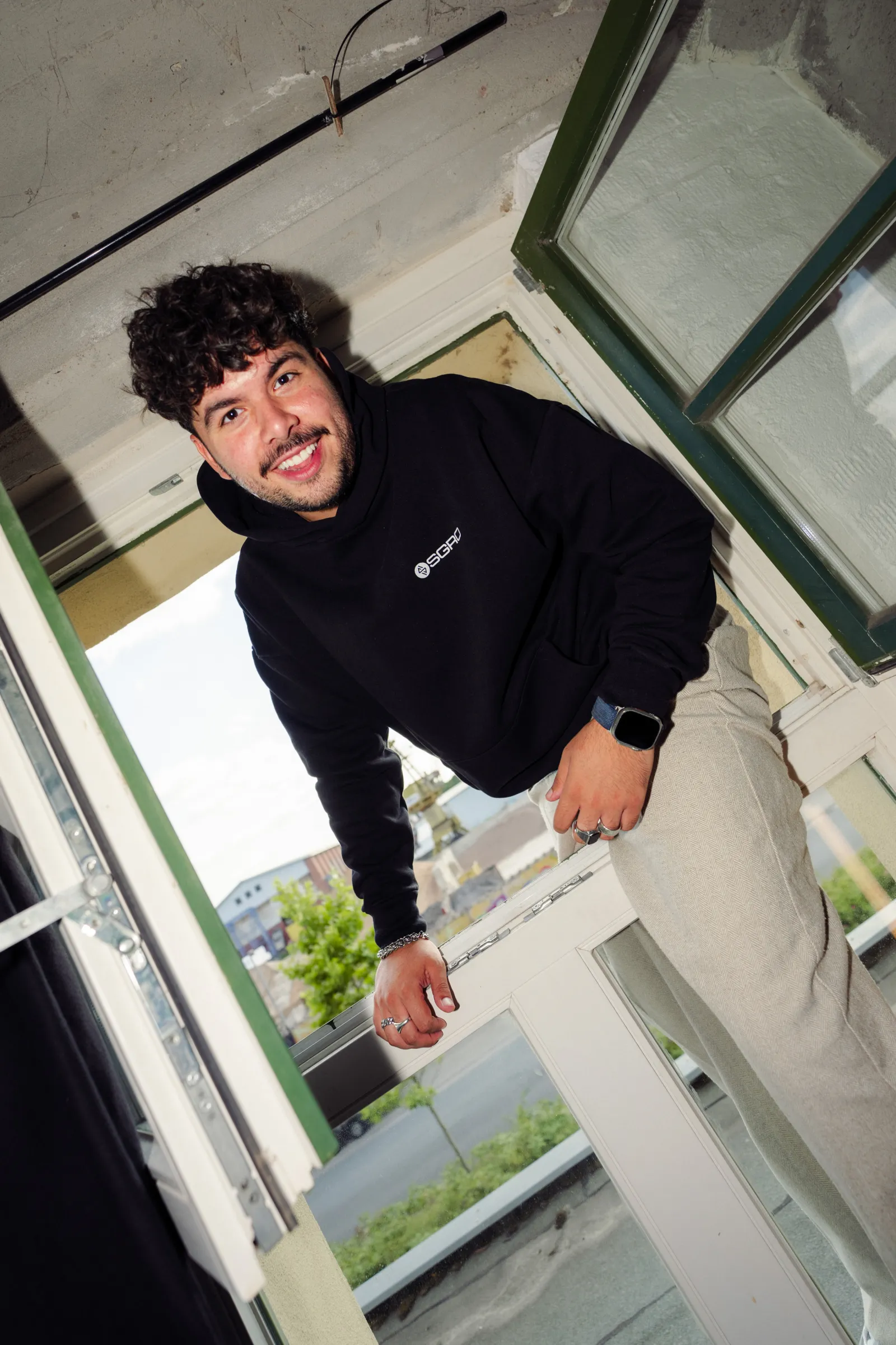 Pasquale lehnt sich im Heavy Hoodie aus dem Studiofenster
